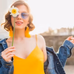 bright-portrait-beautiful-woman-holding-flower-yellow-dress-denim-jacket-hipster-style-summer-fashion-trend-smile-trendy-sunglasses_285396-4532
